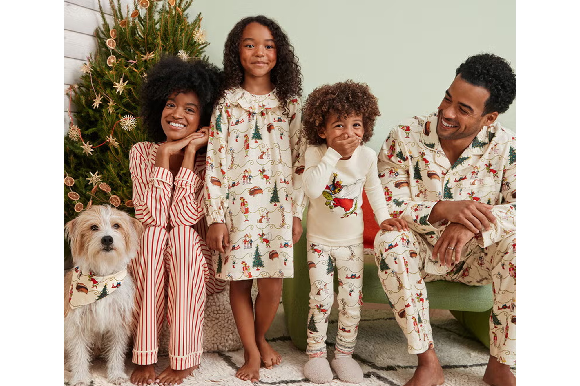 A family and their dog in matching Grinch pajamas next to a Christmas tree.