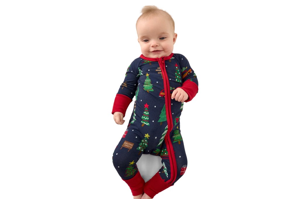 Baby wearing a dark blue Christmas tree themed footie with red cuffs and zipper.