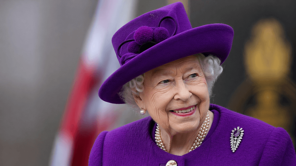 Smiling elderly woman in a purple hat and coat, wearing pearls and a brooch outdoorsan elegant royal-like look (no identity implied)